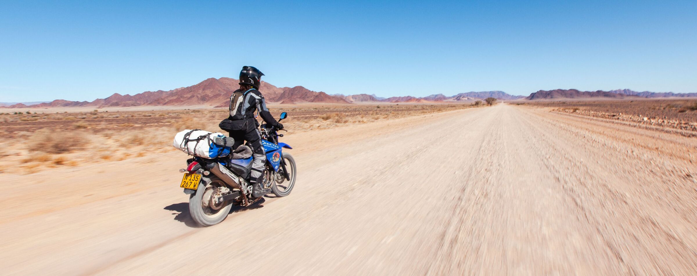 An adventurer on a fully loaded enduro motorcycle rides along an endless, dusty trail through the stunning desert landscape.