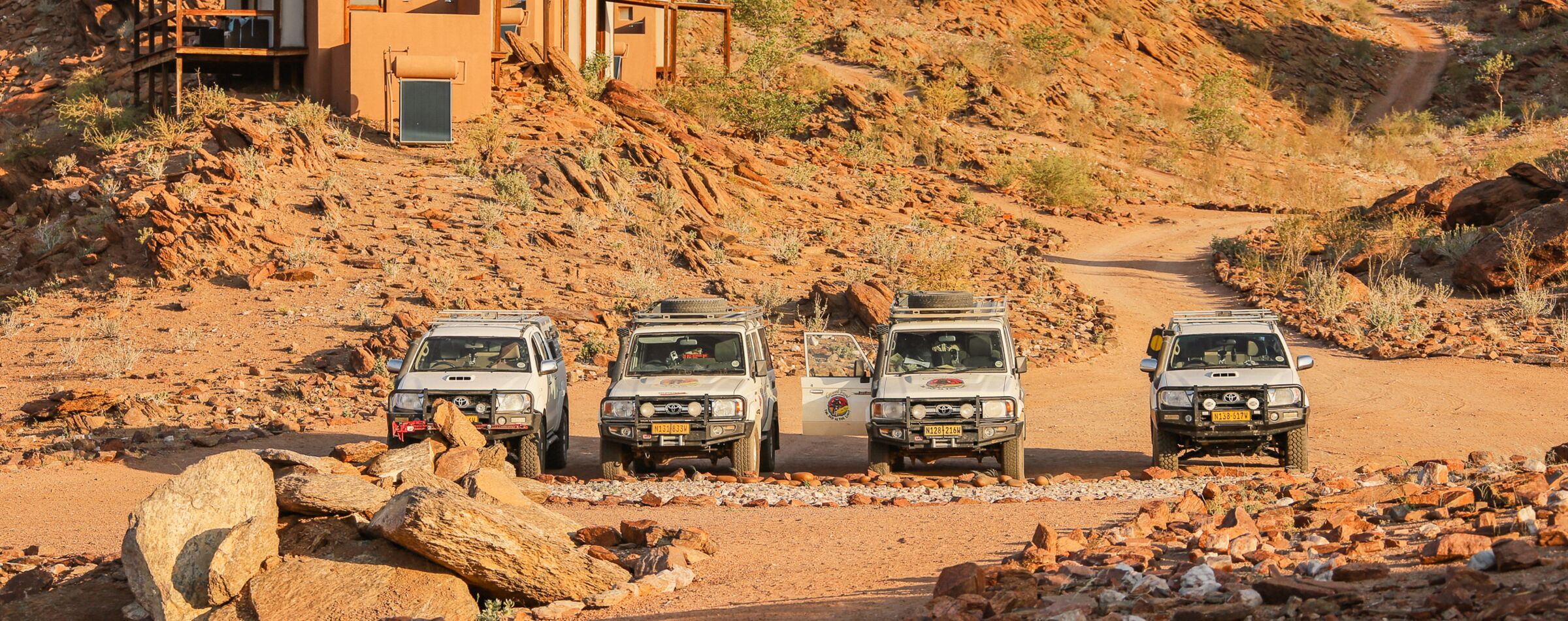 Four 4x4 offroad vehicles parked in front of a lodge in Namibia’s desert landscape. The perfect base for a Gravel Travel adventure.