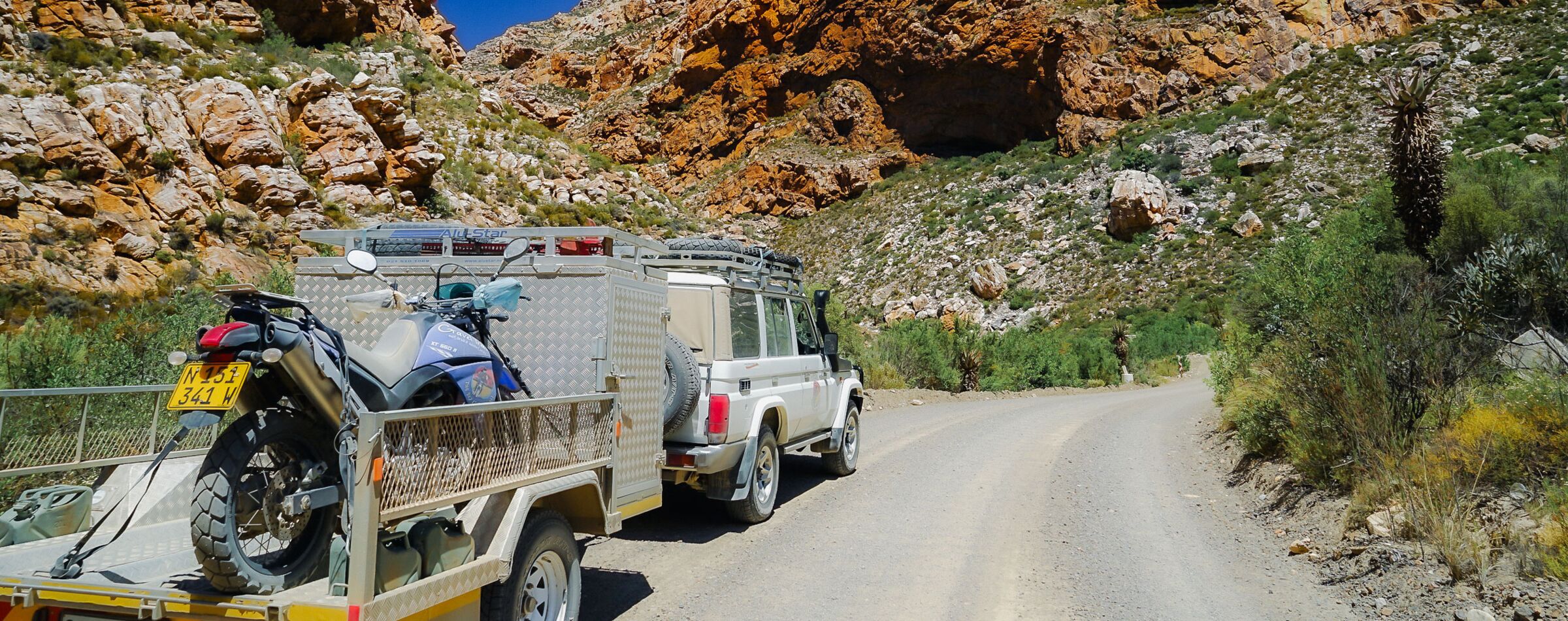 4x4 vehicle with a trailer carrying a motorcycle on a winding gravel road in South Africa. Exploring with Gravel Travel on an offroad adventure.