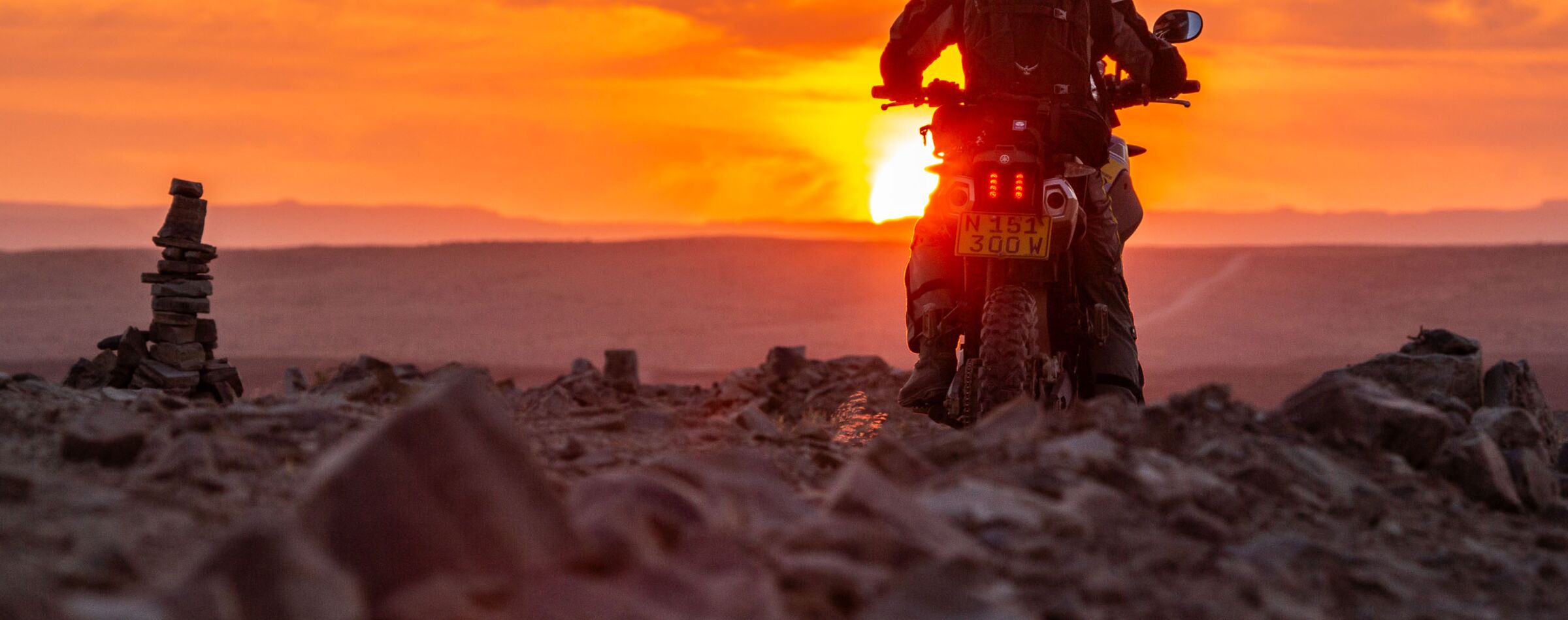 A motorcyclist rides through rocky terrain at sunset in Namibia, capturing the adventure spirit – Gravel Travel.