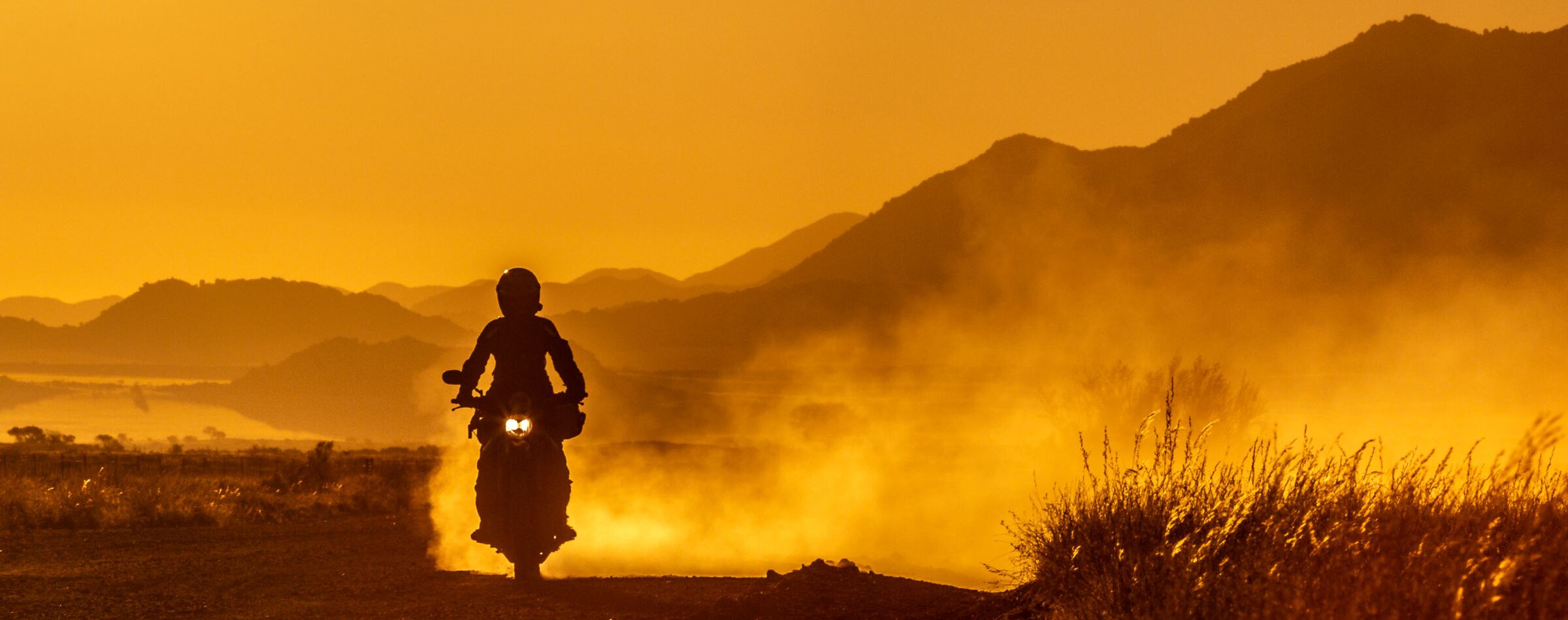 A motorcyclist rides into the sunset, kicking up dust on an off-road adventure with Gravel Travel in Namibia.