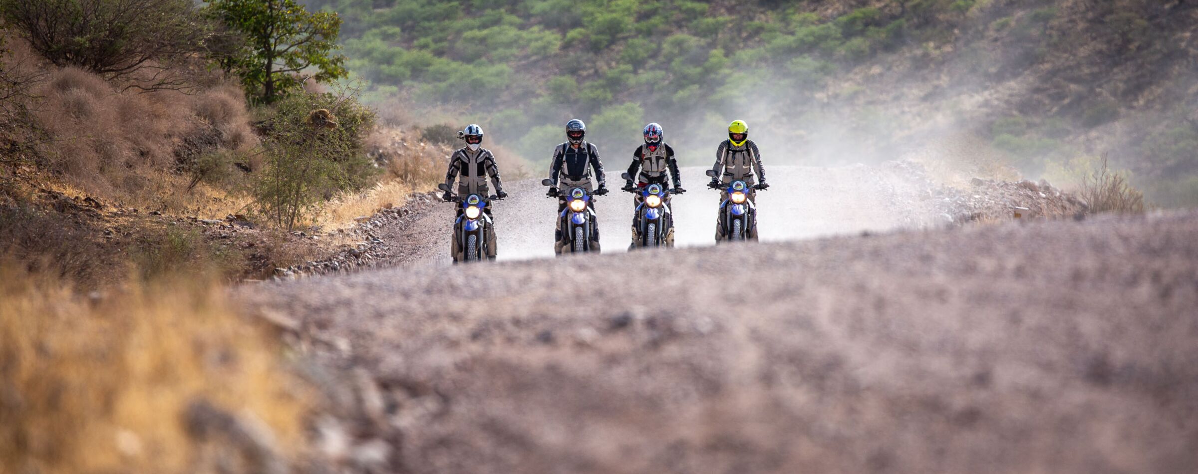 Four motorcyclists riding on a dusty gravel road in Namibia. Offroad experience with Gravel Travel through Africa's vast landscapes.
